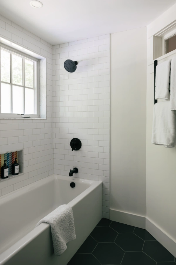 Bathtub and shower combination with white subway tile walls, matte black fixtures, hex tile flooring, and window light